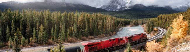 Red long freight train on railway passing through autumn valley with mountain at Morant's Curve, Calgary, Canada