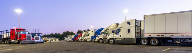 Different make and models big rigs semi trucks with semi trailers standing in row on truck stop parking lot for rest and comply with the movement according to the schedule for successful delivery