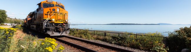 White Rock, Greater Vancouver, British Columbia, Canada - July 25, 2021: A freight train riding through the city by the beach during a colorful summer evening.