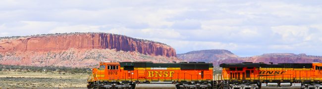 Thoreau, New Mexico, United States - May 24, 2015: Two engines of a BNSF freight train on straight track in the desert in front of rock formations.